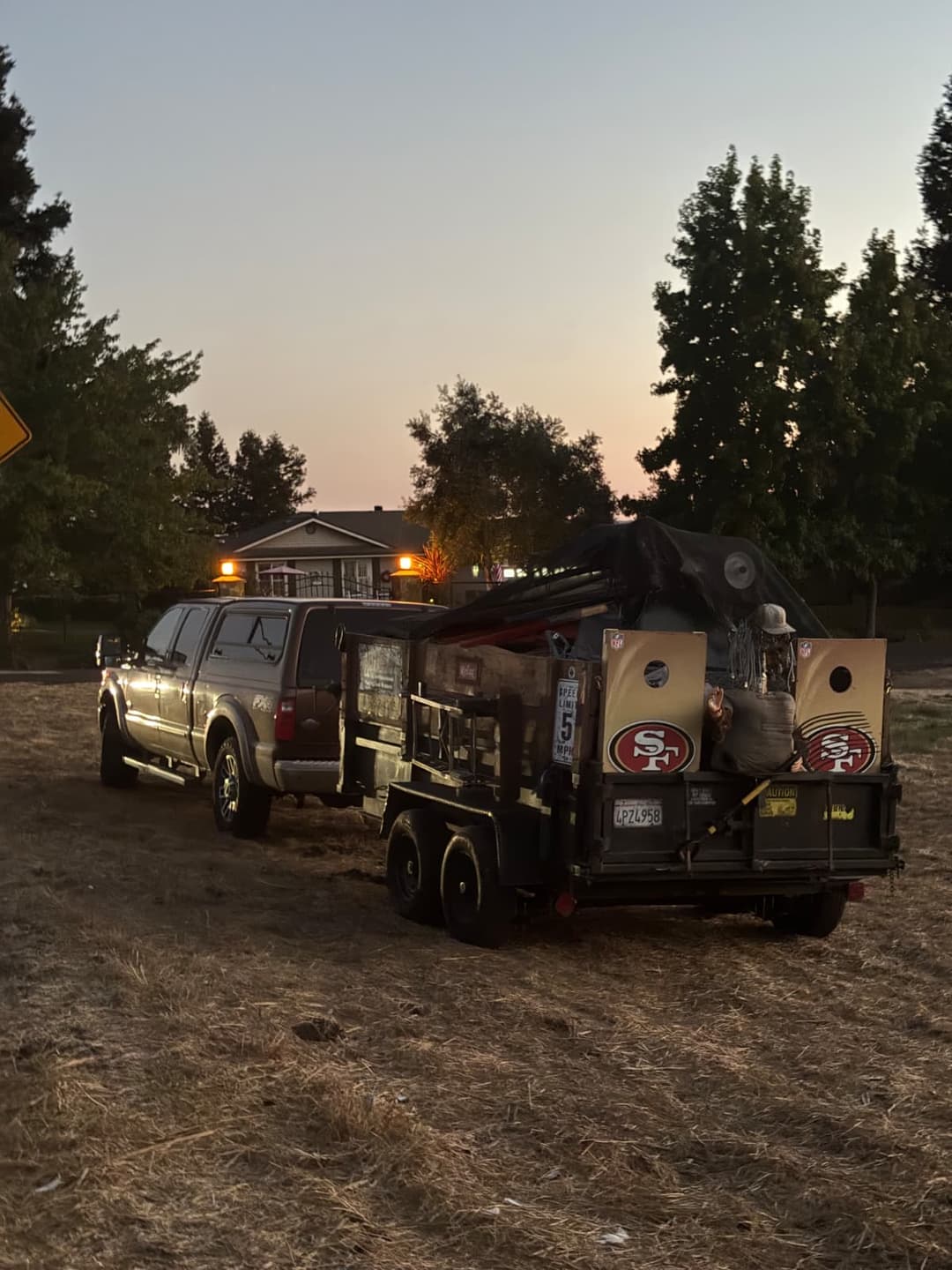 Hauling truck and trailer loaded with debris parked at residential property at dusk.